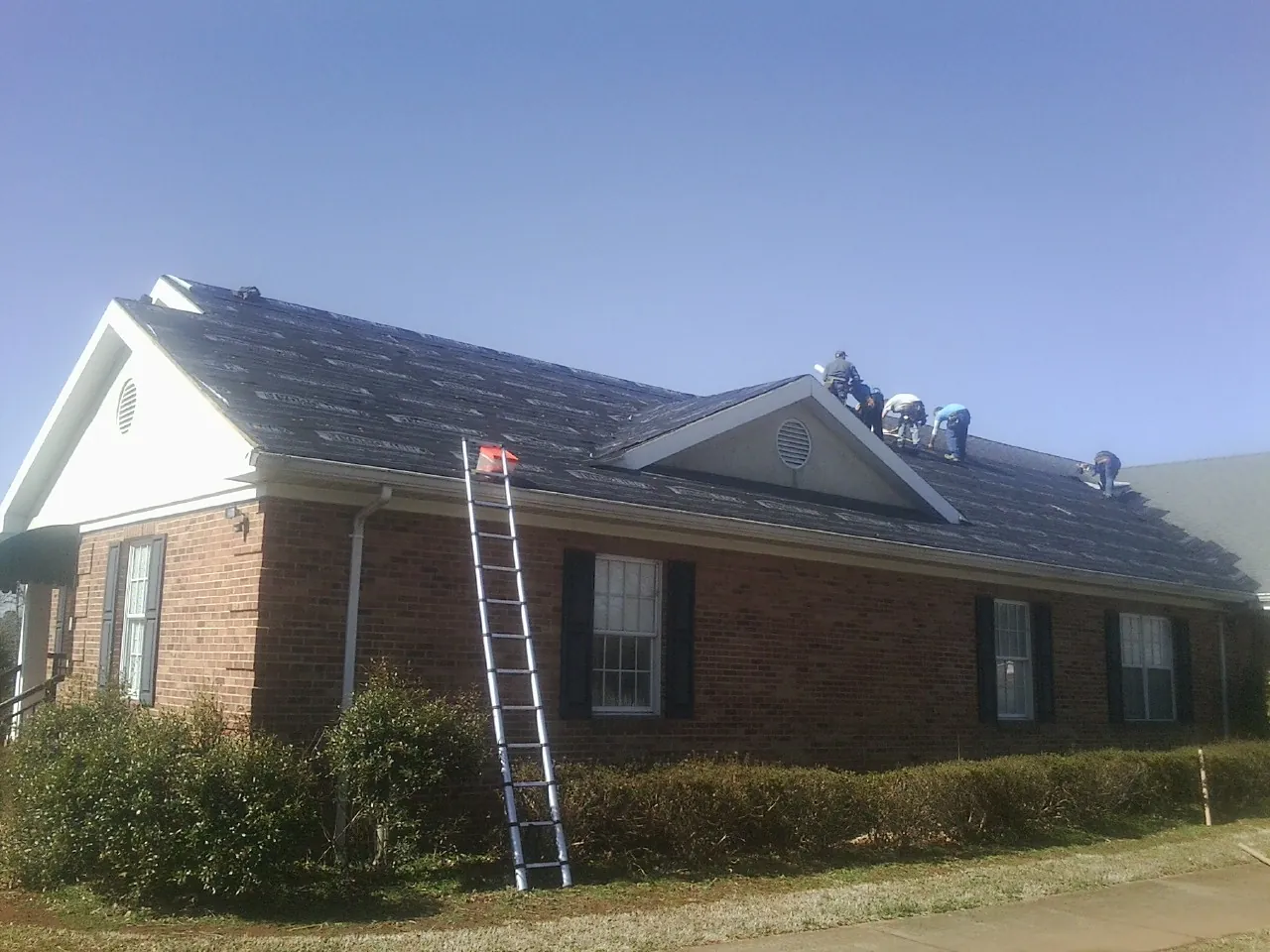 Crew tearing shingles off a brick ranch roof with a ladder set — Emergency Roof Repair work by our crew in Orviston