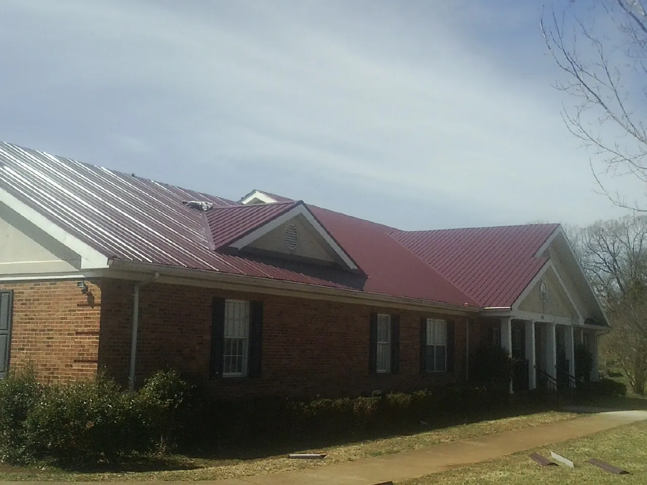 Red metal roof with gabled entries on a long brick building, from a Hail Damage Roof Repair job in Orviston