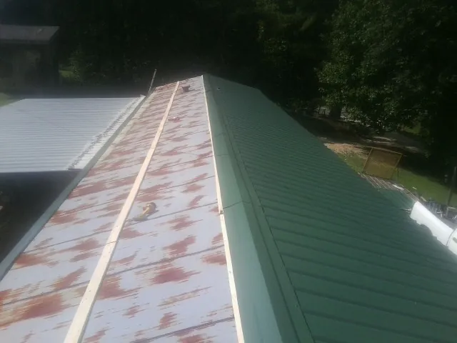 Old rusted panels beside newly installed green metal roofing — Wind Damage Roof Repair by Roofing Brothers in Orviston