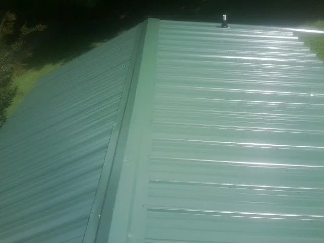 New green metal panels meeting at the ridge of a roof — Flat Roof Repair work by our crew in Orviston