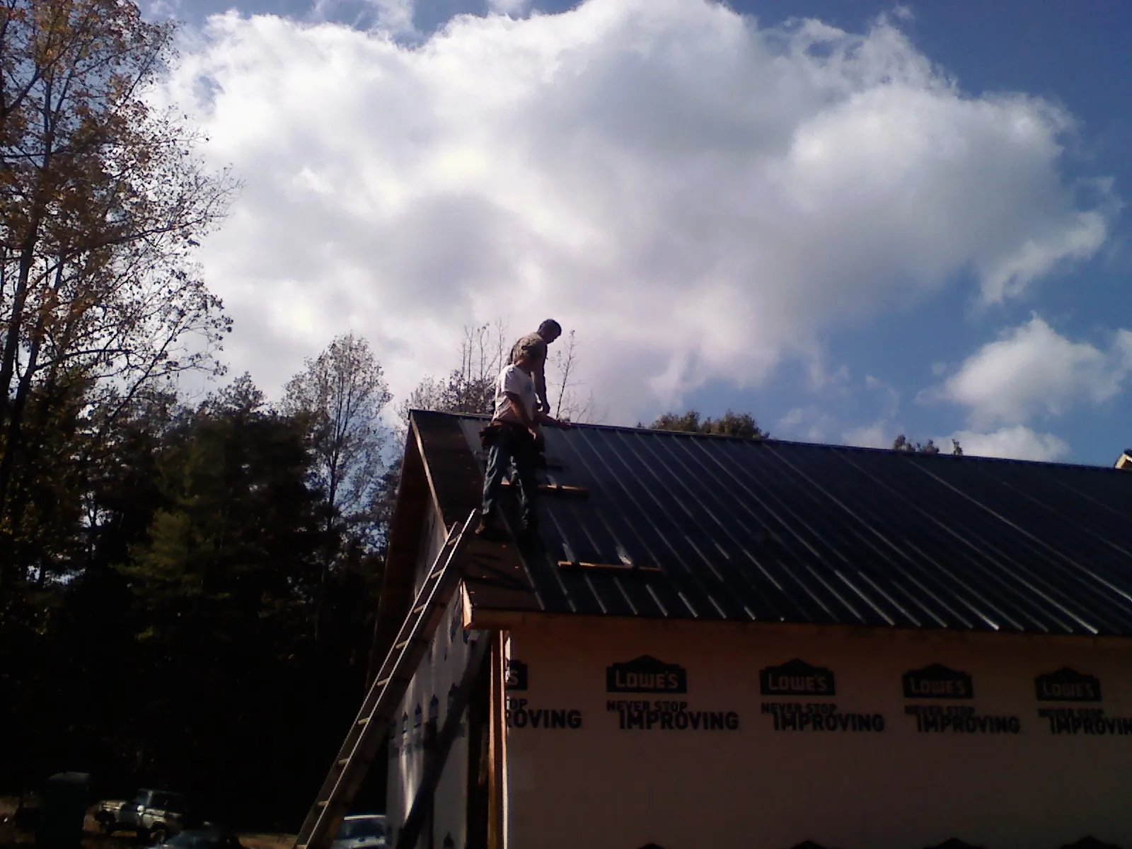 Roofer fastening dark metal panels high against a cloudy sky, from a Roof Inspection job in Orviston
