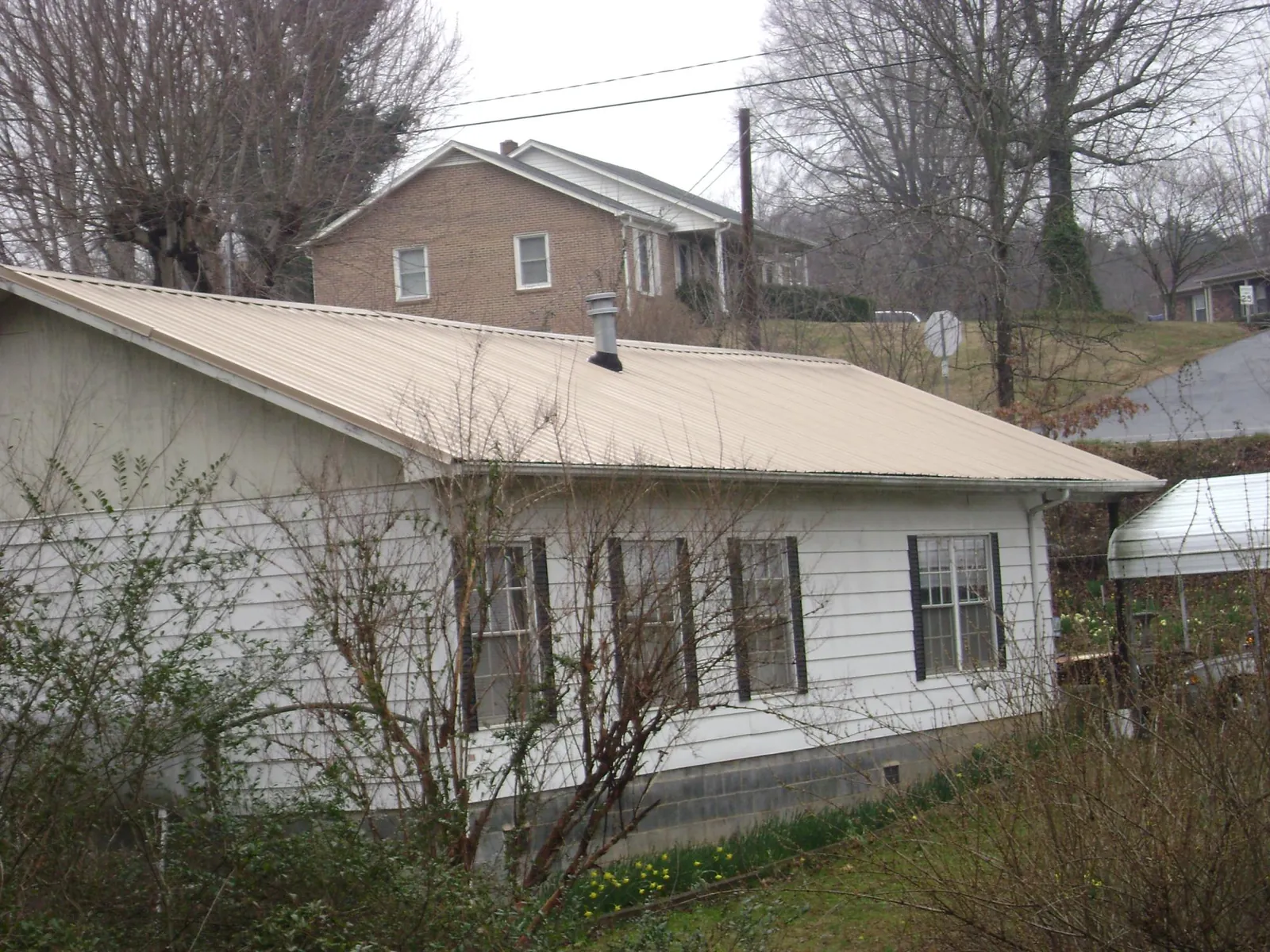 Tan metal roof on a white sided house set into a hillside — Commercial Roofing by Roofing Brothers in Orviston
